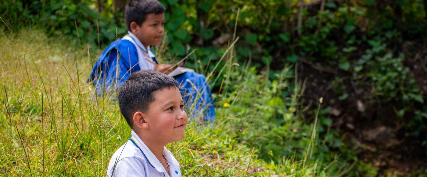 Dos estudiantes de uniforme escriben en sus cuadernos al aire libre, en el campo antioqueÃ±o