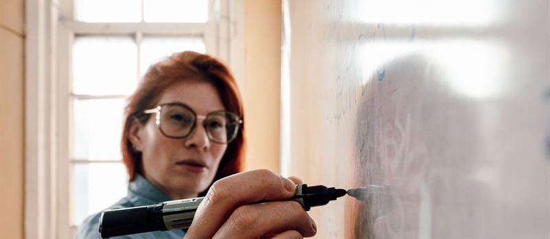 Docente escribiendo en el tablero de su salón