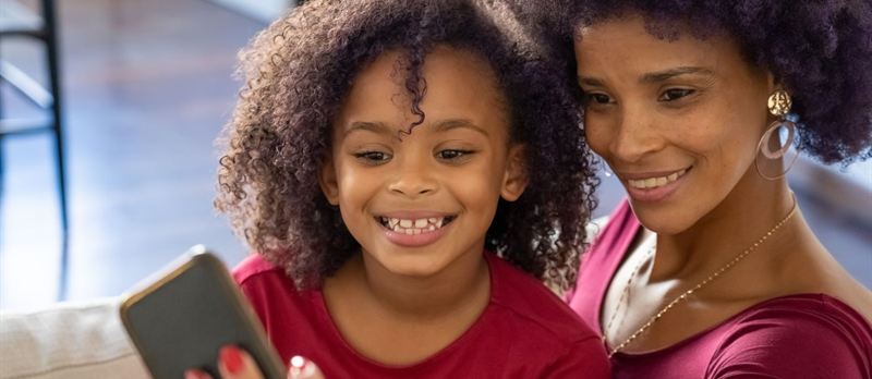 Madre e hija sonríen mirando juntas el celular